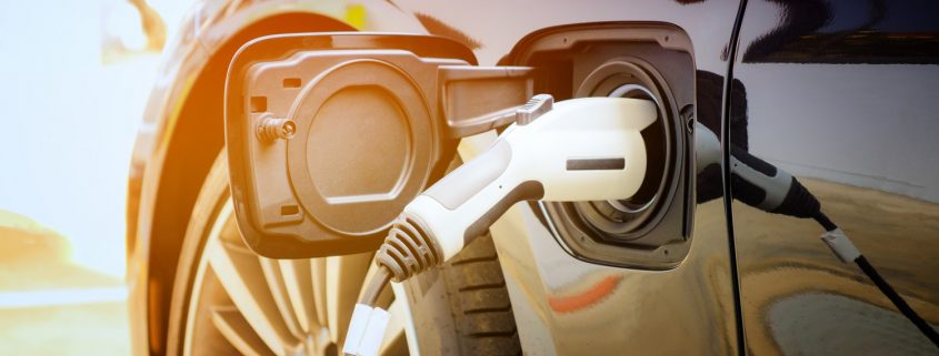 为现代电动汽车电池充电的街道是汽车的未来，特写是将电源插入正在充电的电动汽车进行混合动力。汽车燃料的新时代。